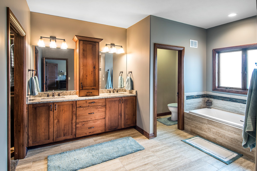 Photo of a large transitional master bathroom in Omaha with an undermount sink, shaker cabinets, dark wood cabinets, granite benchtops, a drop-in tub, a curbless shower, beige tile, ceramic tile, beige walls, ceramic floors, a one-piece toilet, grey floor, an open shower and an enclosed toilet.