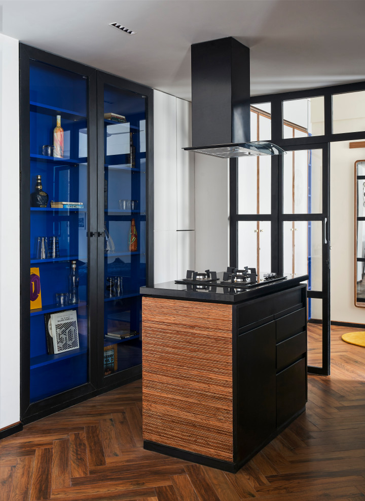Small midcentury home bar in Mumbai with glass-front cabinets, blue cabinets, granite benchtops, porcelain floors, brown floor and black benchtop.