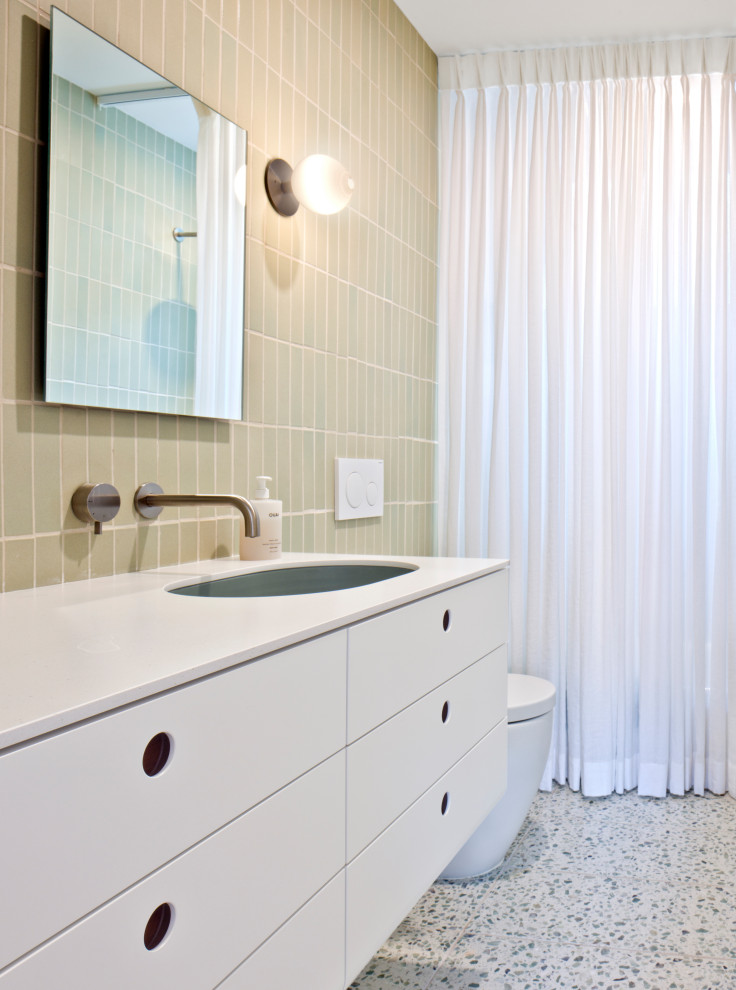 На фото: маленькая ванная комната в стиле модернизм с плоскими фасадами, белыми фасадами, ванной в нише, зеленой плиткой, керамической плиткой, зелеными стенами, полом из терраццо, врезной раковиной, столешницей из кварцита, зеленым полом, шторкой для ванной, белой столешницей, тумбой под одну раковину и встроенной тумбой для на участке и в саду