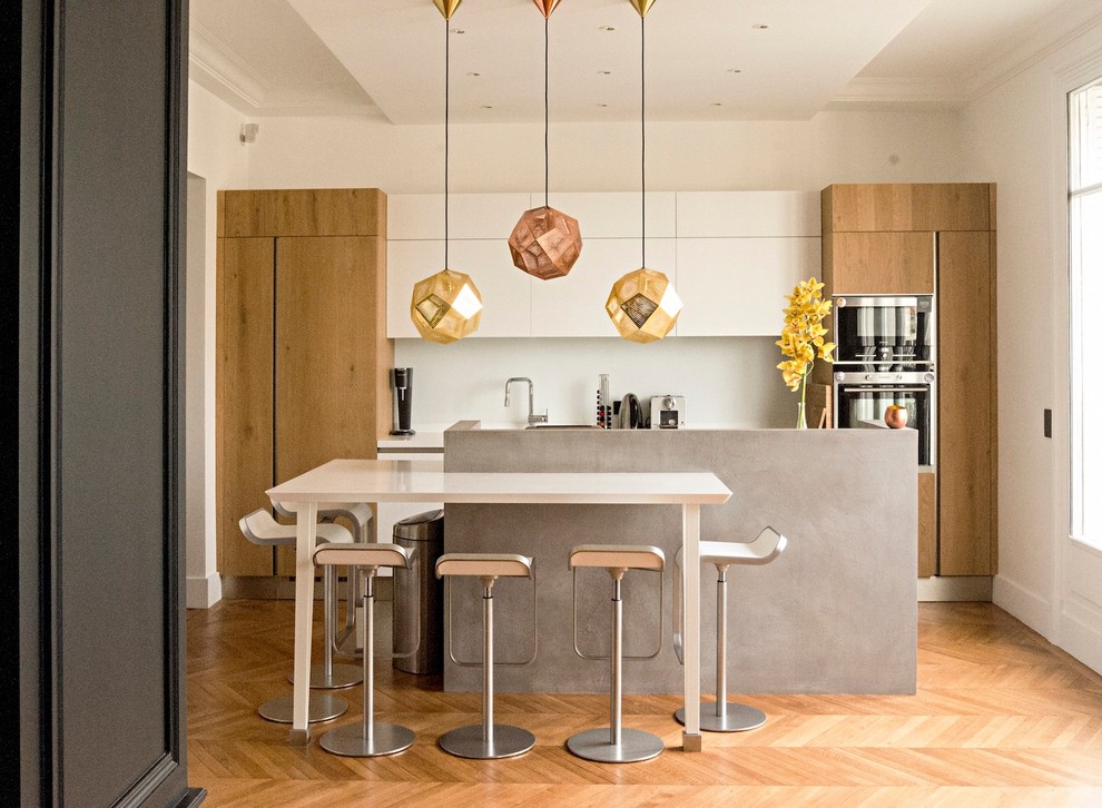Inspiration for a large contemporary galley open plan kitchen in Paris with white splashback, panelled appliances, light hardwood floors, with island and white cabinets.