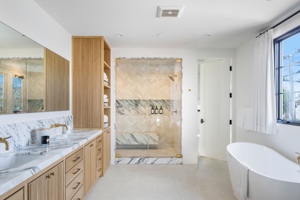 This is an example of a large mediterranean sauna bathroom in Los Angeles with beaded cabinets, light wood cabinets, a freestanding bath, a double shower, a one-piece toilet, multi-coloured tiles, marble tiles, white walls, limestone flooring, a submerged sink, marble worktops, white floors, a hinged door, multi-coloured worktops, a shower bench, double sinks and a built in vanity unit.