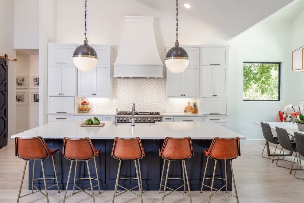 Inspiration for a large u-shaped light wood floor and beige floor eat-in kitchen remodel in Austin with a farmhouse sink, recessed-panel cabinets, white cabinets, quartzite countertops, white backsplash, ceramic backsplash, paneled appliances, an island and white countertops