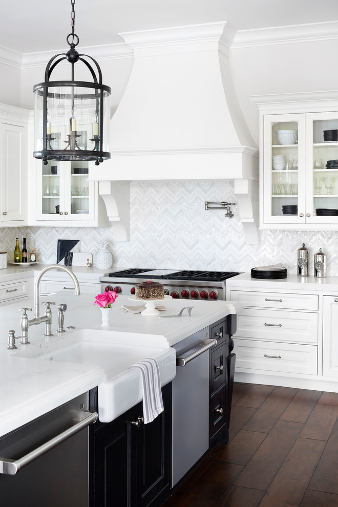 Photo of a transitional kitchen in Miami with a farmhouse sink, raised-panel cabinets, white cabinets, white splashback, stainless steel appliances, dark hardwood floors, with island, brown floor and white benchtop.