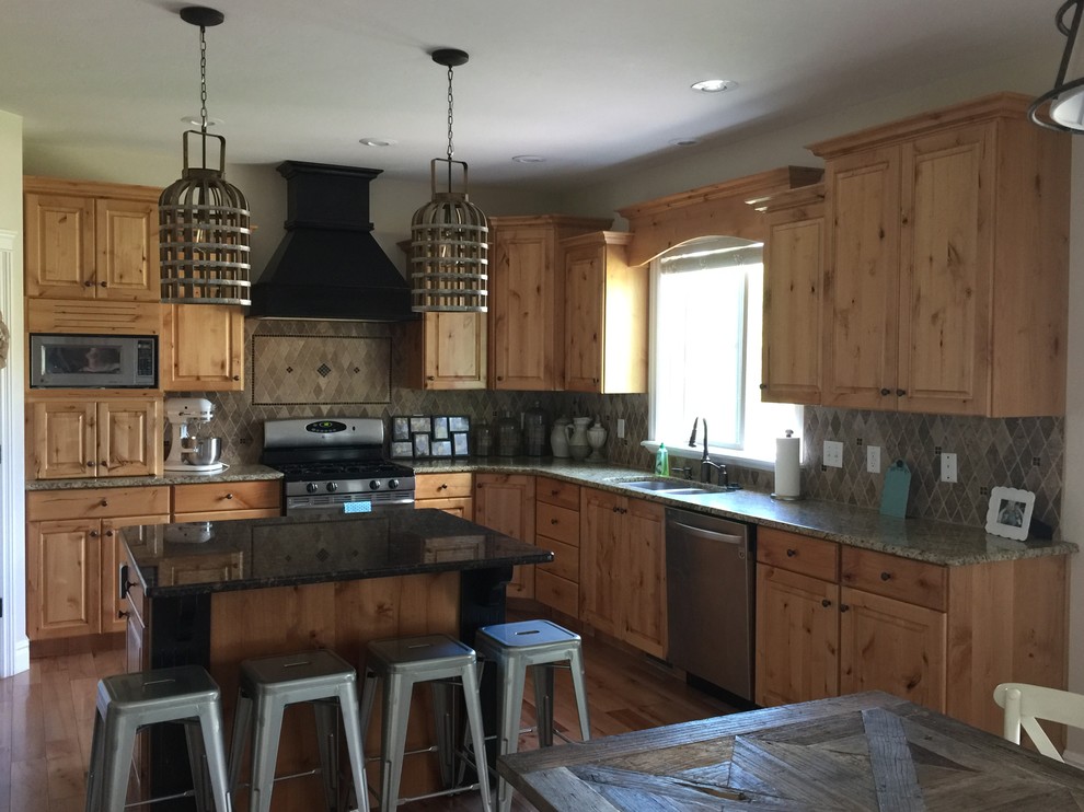 Example of a mid-sized mountain style l-shaped medium tone wood floor and brown floor eat-in kitchen design in Austin with a double-bowl sink, raised-panel cabinets, medium tone wood cabinets, granite countertops, brown backsplash, ceramic backsplash, stainless steel appliances and an island