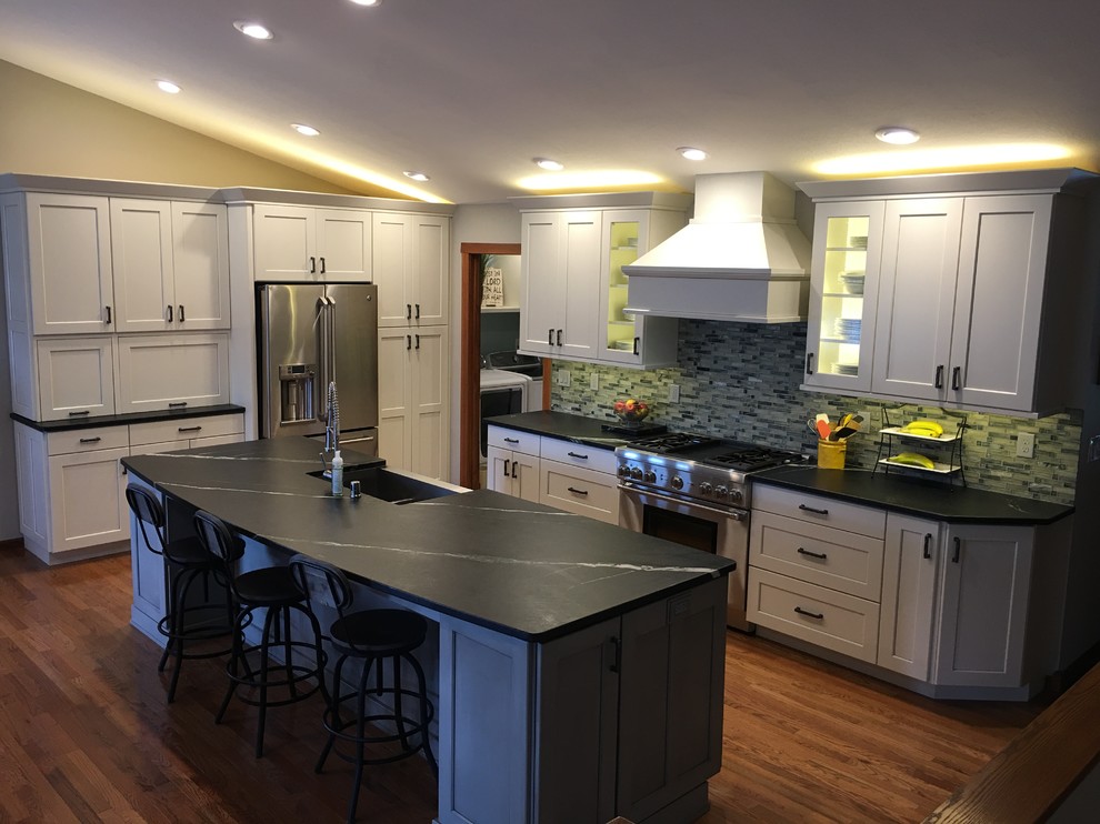 Eat-in kitchen - large transitional l-shaped dark wood floor and brown floor eat-in kitchen idea with a farmhouse sink, white cabinets, stainless steel appliances, an island, shaker cabinets, quartz countertops and gray backsplash