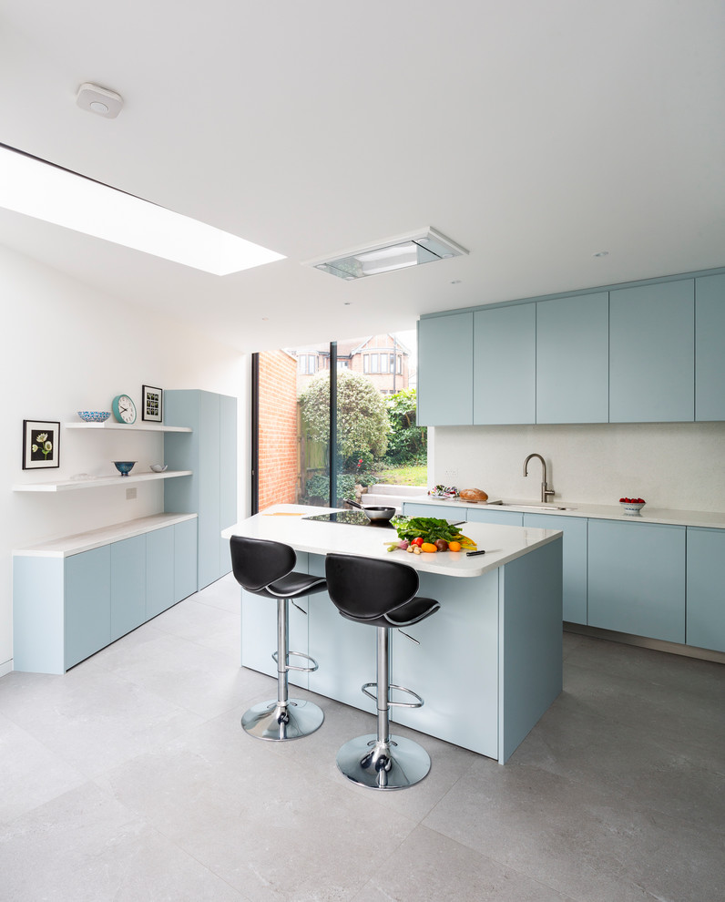 This is an example of a mid-sized contemporary kitchen in London with flat-panel cabinets, blue cabinets, with island, white benchtop, white splashback, an undermount sink and grey floor.