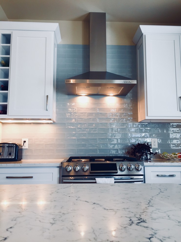 Mid-sized transitional light wood floor kitchen photo with an undermount sink, shaker cabinets, white cabinets, quartz countertops, blue backsplash, glass tile backsplash, stainless steel appliances and an island