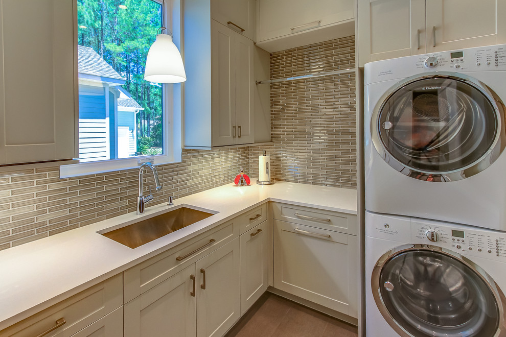 Mid-sized transitional l-shaped dedicated laundry room in Orange County with an undermount sink, shaker cabinets, white cabinets, solid surface benchtops, beige walls, medium hardwood floors and a stacked washer and dryer.