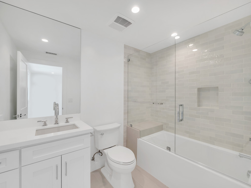 This is an example of a mid-sized country kids bathroom in Los Angeles with shaker cabinets, white cabinets, a drop-in tub, a shower/bathtub combo, a two-piece toilet, white tile, ceramic tile, white walls, porcelain floors, an undermount sink, limestone benchtops, beige floor, a hinged shower door, white benchtops, a shower seat, a single vanity and a built-in vanity.