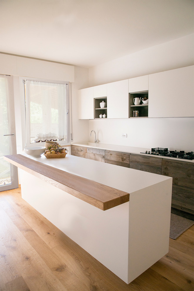 This is an example of a contemporary eat-in kitchen in Venice with light hardwood floors, with island, an integrated sink, flat-panel cabinets, white cabinets, solid surface benchtops and white splashback.