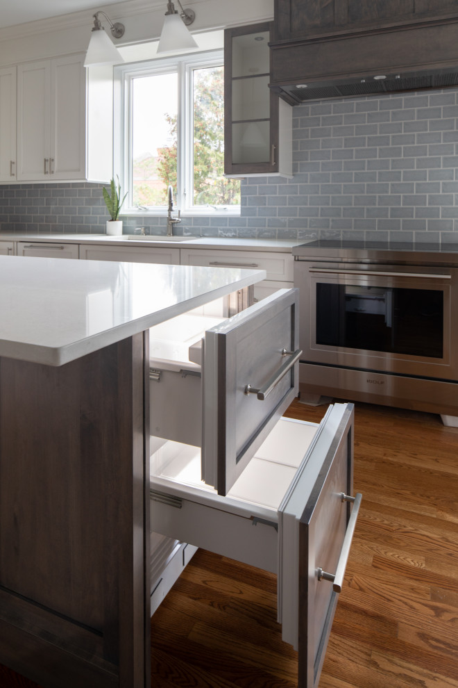 Inspiration for a mid-sized transitional l-shaped medium tone wood floor and brown floor enclosed kitchen remodel with an undermount sink, shaker cabinets, white cabinets, quartz countertops, blue backsplash, subway tile backsplash, stainless steel appliances, an island and white countertops