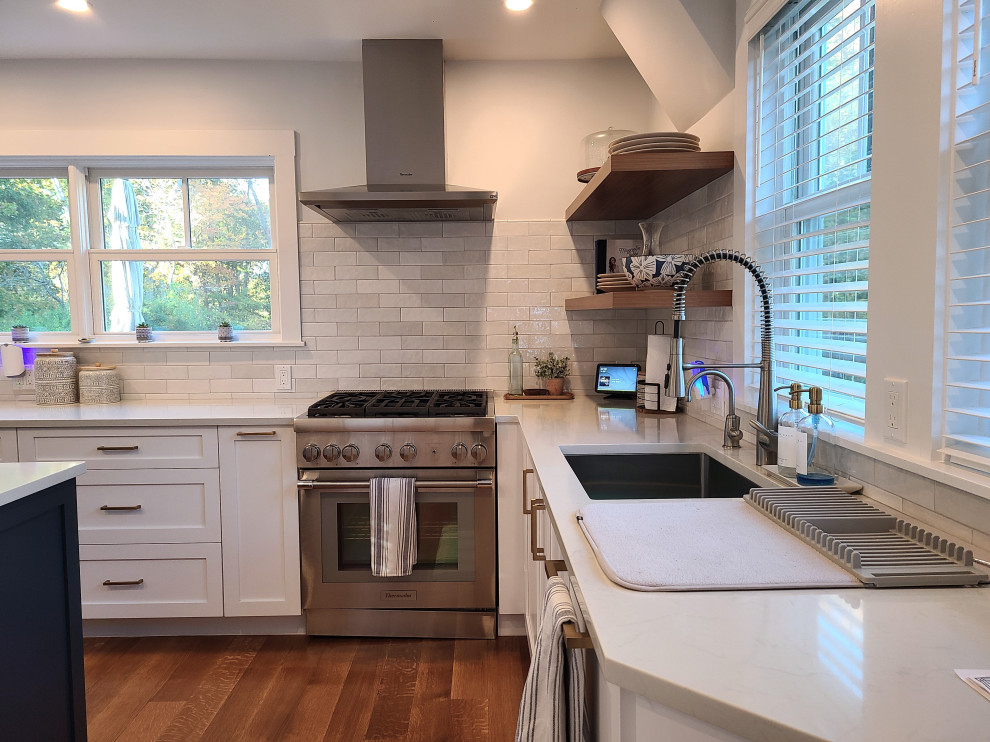 Large transitional u-shaped medium tone wood floor and brown floor eat-in kitchen photo in Boston with an undermount sink, recessed-panel cabinets, white cabinets, white backsplash, subway tile backsplash, stainless steel appliances, an island and white countertops