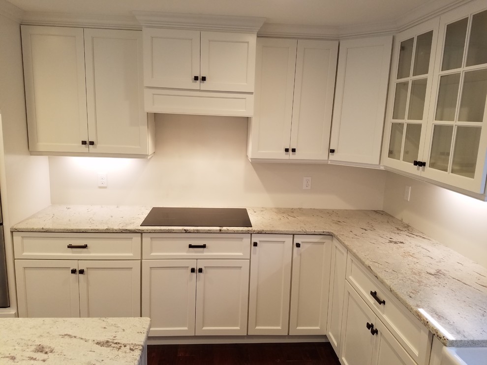 Example of a mid-sized transitional l-shaped dark wood floor and brown floor eat-in kitchen design with a farmhouse sink, shaker cabinets, white cabinets, granite countertops, white backsplash, subway tile backsplash, stainless steel appliances and an island