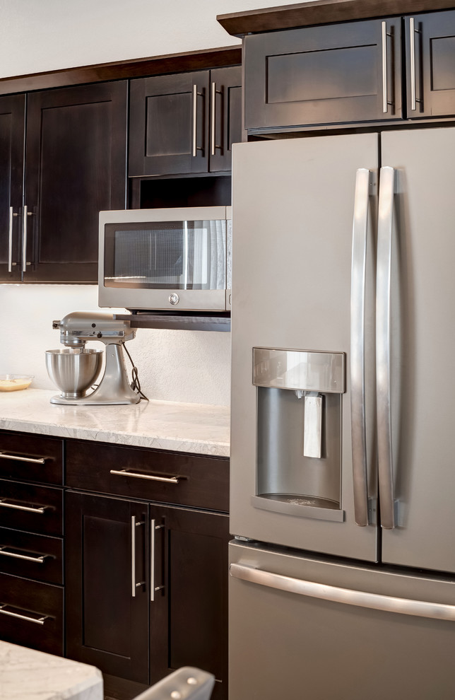 Large transitional l-shaped medium tone wood floor open concept kitchen photo with a double-bowl sink, shaker cabinets, dark wood cabinets, quartzite countertops, stainless steel appliances and an island