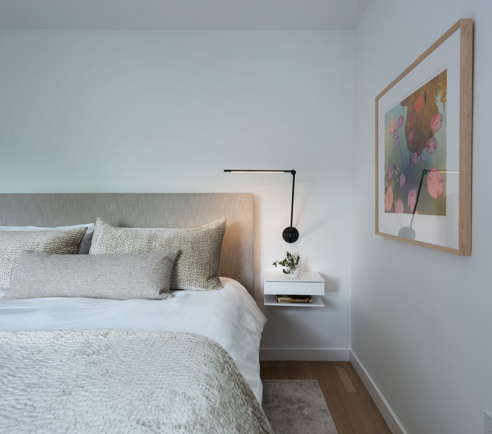 This is an example of a modern bedroom in Boston with white walls and medium hardwood floors.