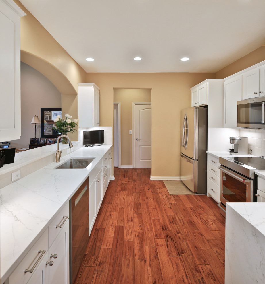 Enclosed kitchen - mid-sized transitional galley medium tone wood floor and brown floor enclosed kitchen idea in Columbus with a single-bowl sink, shaker cabinets, white cabinets, quartz countertops, white backsplash, ceramic backsplash, stainless steel appliances, no island and white countertops
