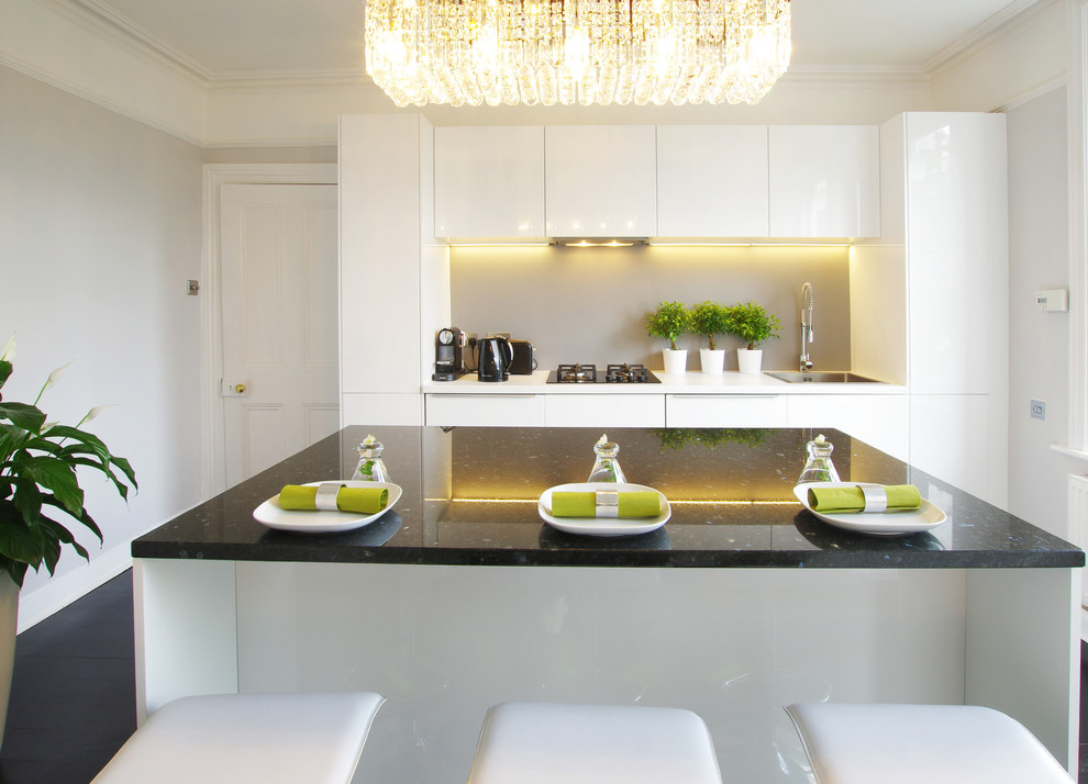 Inspiration for a medium sized contemporary galley enclosed kitchen in London with a built-in sink, flat-panel cabinets, white cabinets, grey splashback, integrated appliances, an island and dark hardwood flooring.