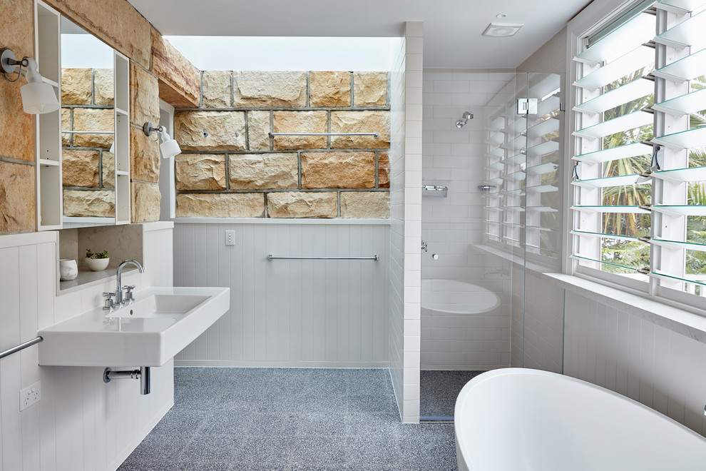 This is an example of a beach style master bathroom in Sydney with white tile, open cabinets, white cabinets, a freestanding tub, an alcove shower, multi-coloured walls, concrete floors, a wall-mount sink, grey floor and a hinged shower door.