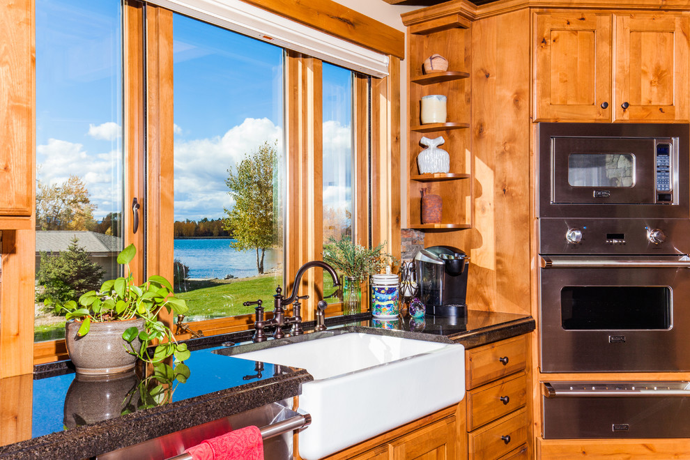 Example of a mid-sized mountain style l-shaped dark wood floor open concept kitchen design with a farmhouse sink, shaker cabinets, medium tone wood cabinets, granite countertops, multicolored backsplash, stone tile backsplash, stainless steel appliances and an island