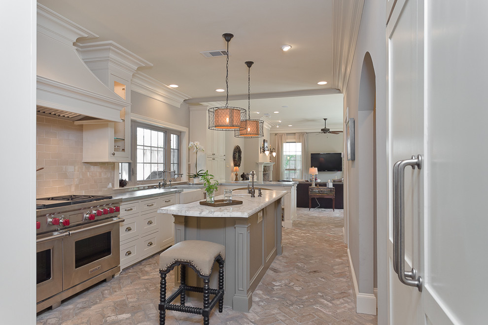 Photo of a mid-sized traditional u-shaped open plan kitchen in Houston with a farmhouse sink, recessed-panel cabinets, white cabinets, marble benchtops, beige splashback, stainless steel appliances, brick floors and with island.