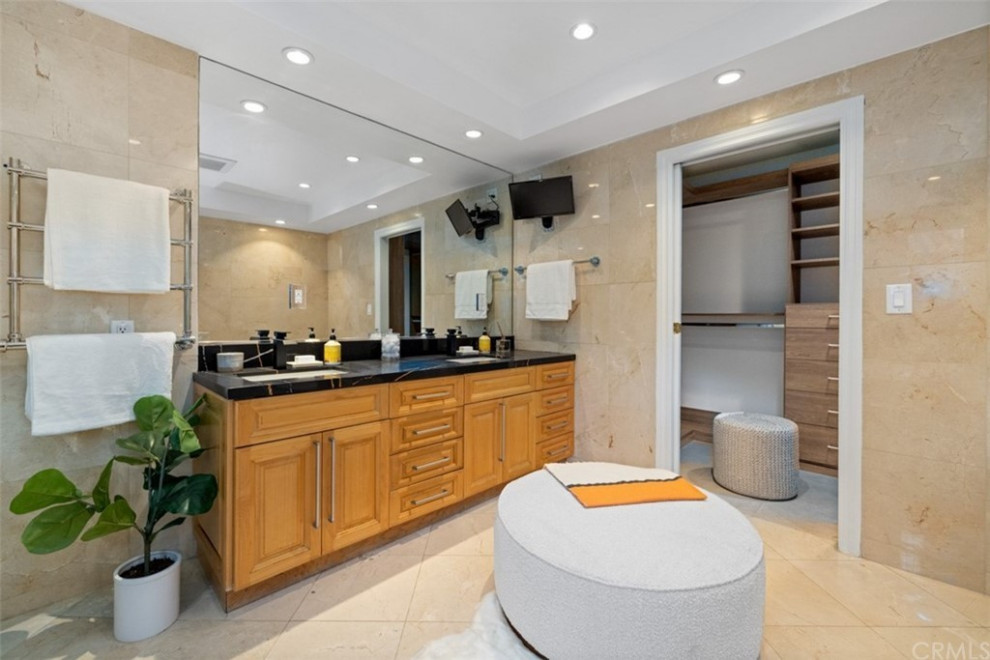 Large modern master bathroom in Los Angeles with shaker cabinets, brown cabinets, a corner tub, a corner shower, a one-piece toilet, beige tile, marble, brown walls, marble floors, a drop-in sink, beige floor, a hinged shower door, black benchtops, a niche, a double vanity, recessed, engineered quartz benchtops and a built-in vanity.