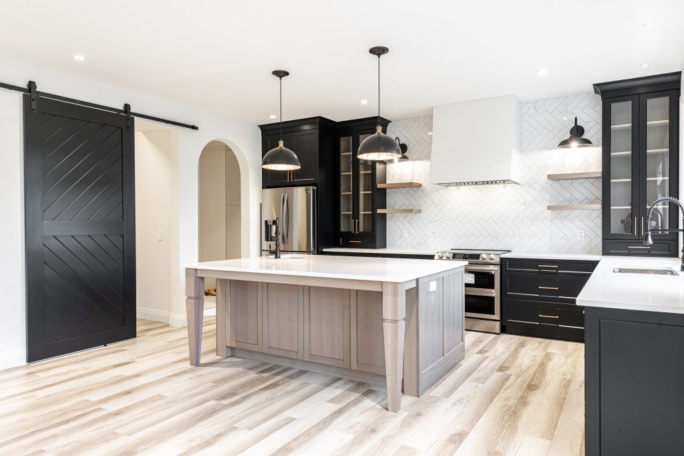 Mid-sized transitional l-shaped laminate floor and brown floor eat-in kitchen photo in Toronto with an undermount sink, recessed-panel cabinets, black cabinets, quartz countertops, white backsplash, ceramic backsplash, stainless steel appliances, an island and white countertops
