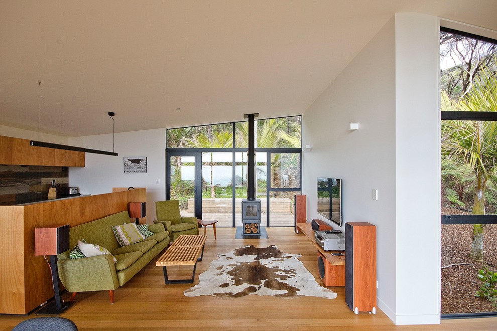 Small beach style open concept living room in Auckland with white walls, light hardwood floors, a wood stove, a stone fireplace surround, no tv and beige floor.