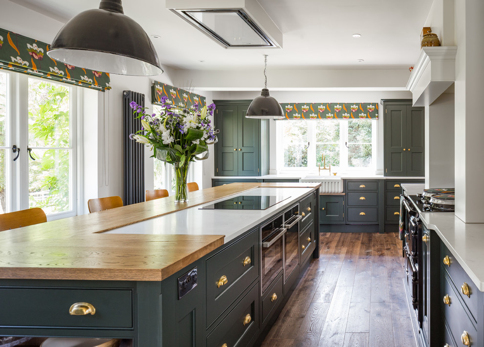 Large transitional u-shaped kitchen in Manchester with shaker cabinets, green cabinets, granite benchtops, white splashback, limestone splashback, with island, white benchtop, a farmhouse sink, medium hardwood floors and brown floor.