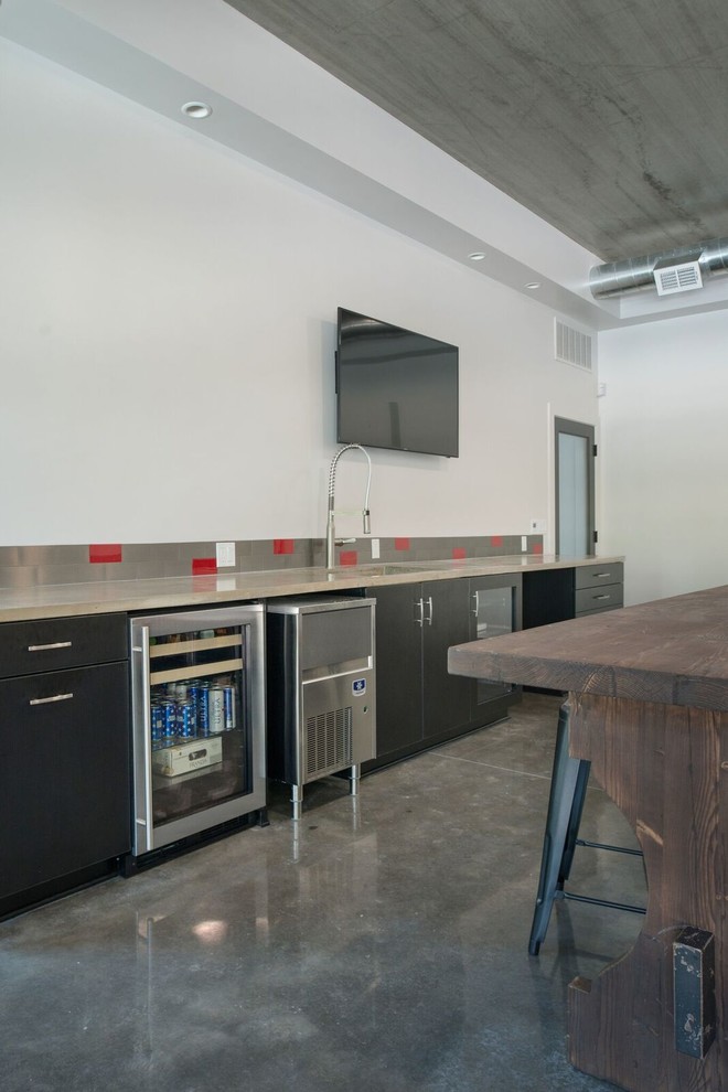 Inspiration for a large industrial single-wall wet bar in Orange County with flat-panel cabinets, concrete floors, an undermount sink, black cabinets, grey splashback, metal splashback and grey floor.