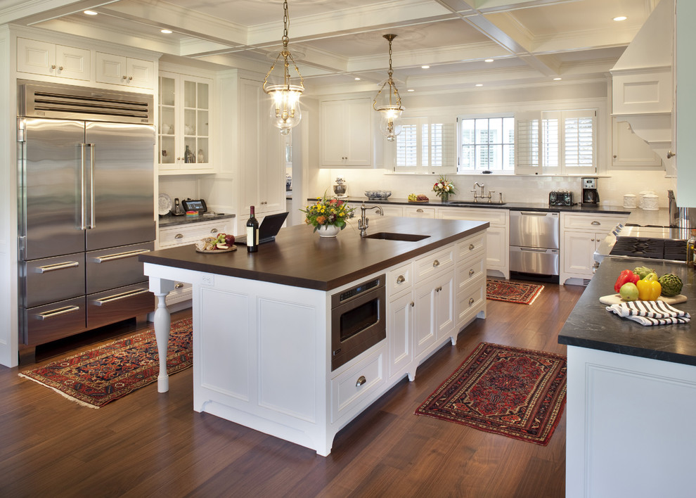 Design ideas for a traditional u-shaped kitchen in Boston with recessed-panel cabinets, stainless steel appliances, soapstone benchtops, white cabinets, an undermount sink, white splashback, subway tile splashback, medium hardwood floors, with island and brown floor.