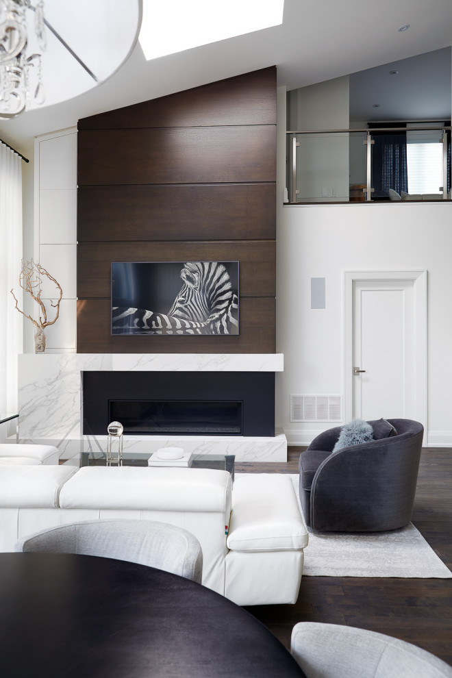 Large contemporary open plan games room in Toronto with white walls, dark hardwood flooring, a standard fireplace, a timber clad chimney breast, a wall mounted tv, brown floors and a vaulted ceiling.