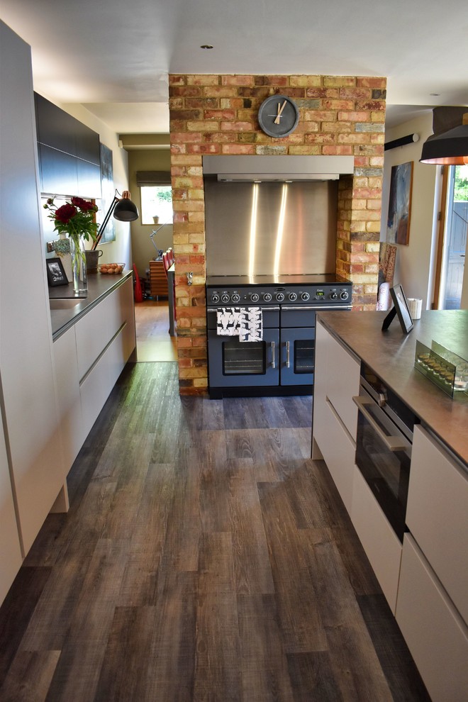Large contemporary kitchen/diner in Cambridgeshire with a submerged sink, flat-panel cabinets, beige cabinets, black appliances, light hardwood flooring, an island and grey worktops.