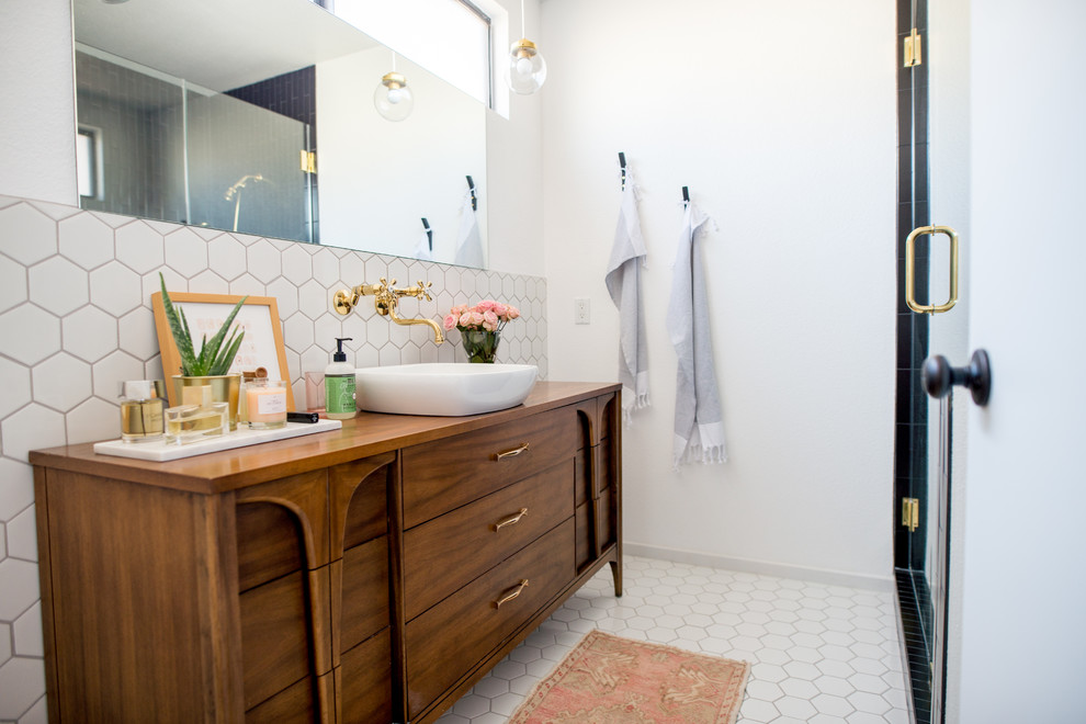 Mid-sized modern master bathroom in Las Vegas with furniture-like cabinets, medium wood cabinets, a corner shower, a one-piece toilet, white tile, porcelain tile, white walls, porcelain floors, a vessel sink, wood benchtops, white floor, a hinged shower door and brown benchtops.