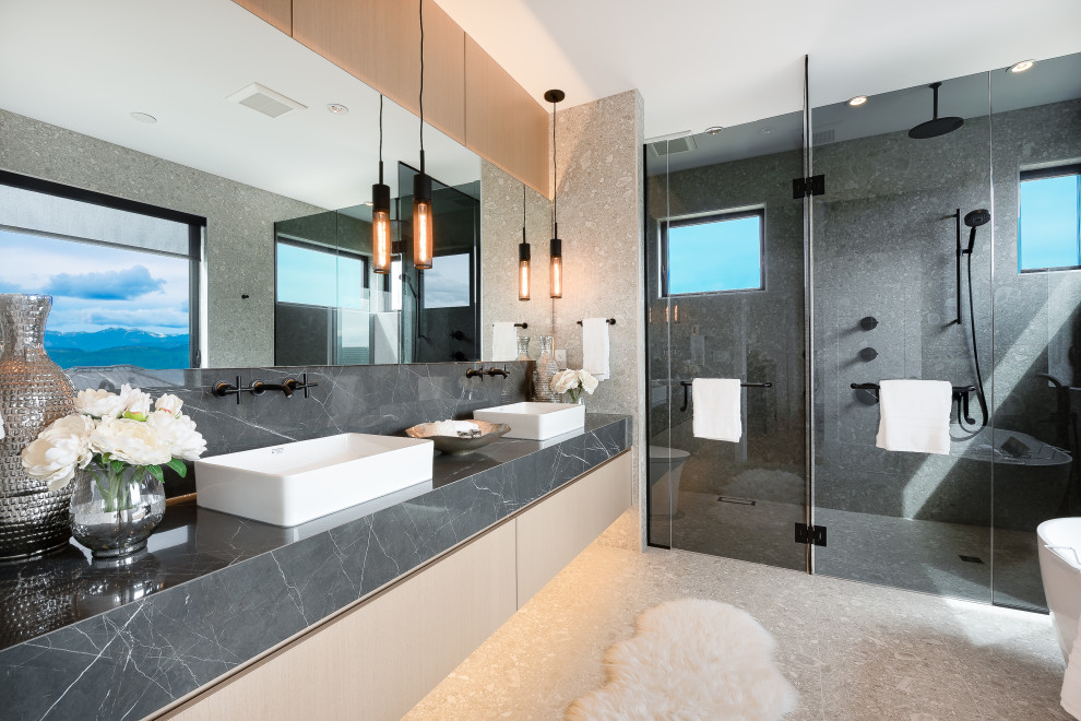 This is an example of a large contemporary master bathroom in Vancouver with flat-panel cabinets, light wood cabinets, an alcove shower, a one-piece toilet, gray tile, porcelain tile, grey walls, porcelain floors, a vessel sink, marble benchtops, grey floor, a hinged shower door, black benchtops, an enclosed toilet, a double vanity and a floating vanity.