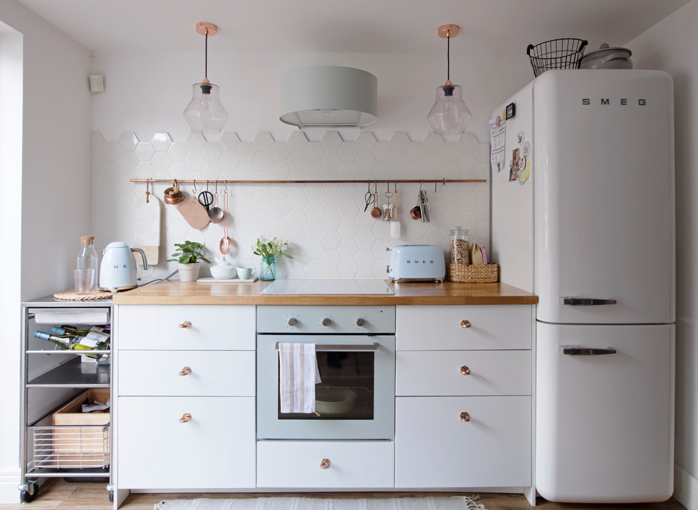 Photo of a scandinavian single-wall kitchen in London with flat-panel cabinets, white cabinets, wood benchtops, white splashback, white appliances, no island and brown benchtop.