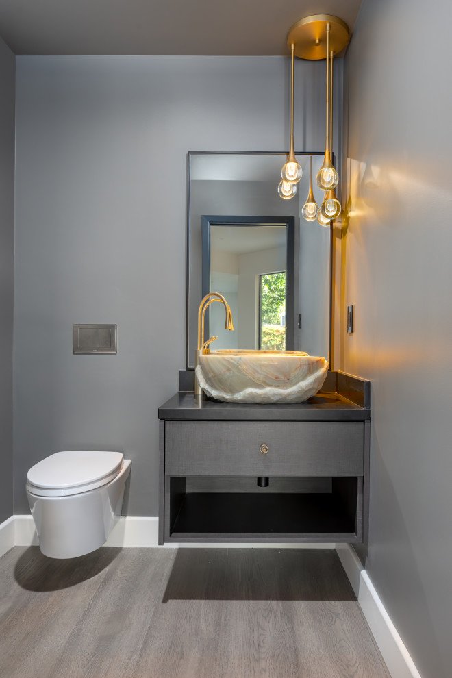 Photo of a contemporary powder room in San Francisco with flat-panel cabinets, grey cabinets, a one-piece toilet, grey walls, medium hardwood floors, a vessel sink, engineered quartz benchtops, brown floor, black benchtops and a floating vanity.