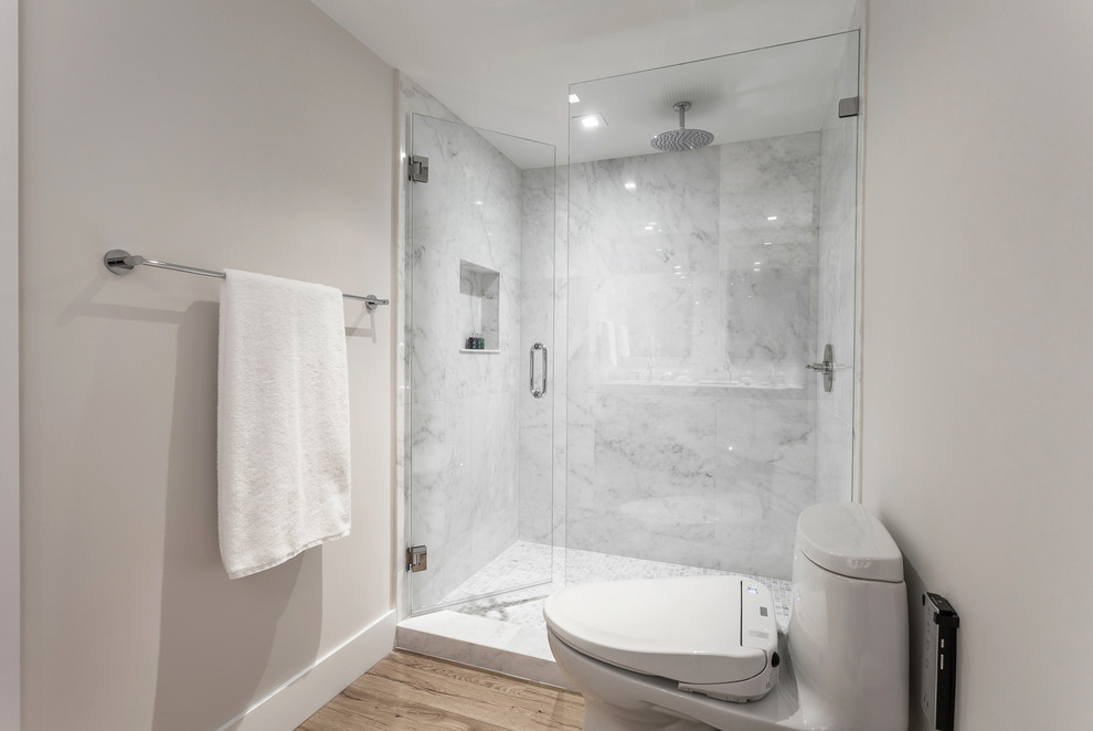 Photo of a mid-sized country master bathroom in Miami with flat-panel cabinets, white cabinets, a one-piece toilet, beige tile, marble, beige walls, laminate floors, an undermount sink, marble benchtops, beige floor, a hinged shower door and white benchtops.