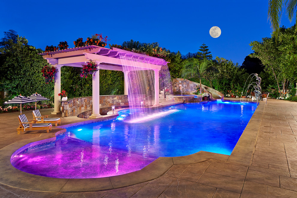 Large mediterranean backyard custom-shaped natural pool in Los Angeles with stamped concrete and a water slide.