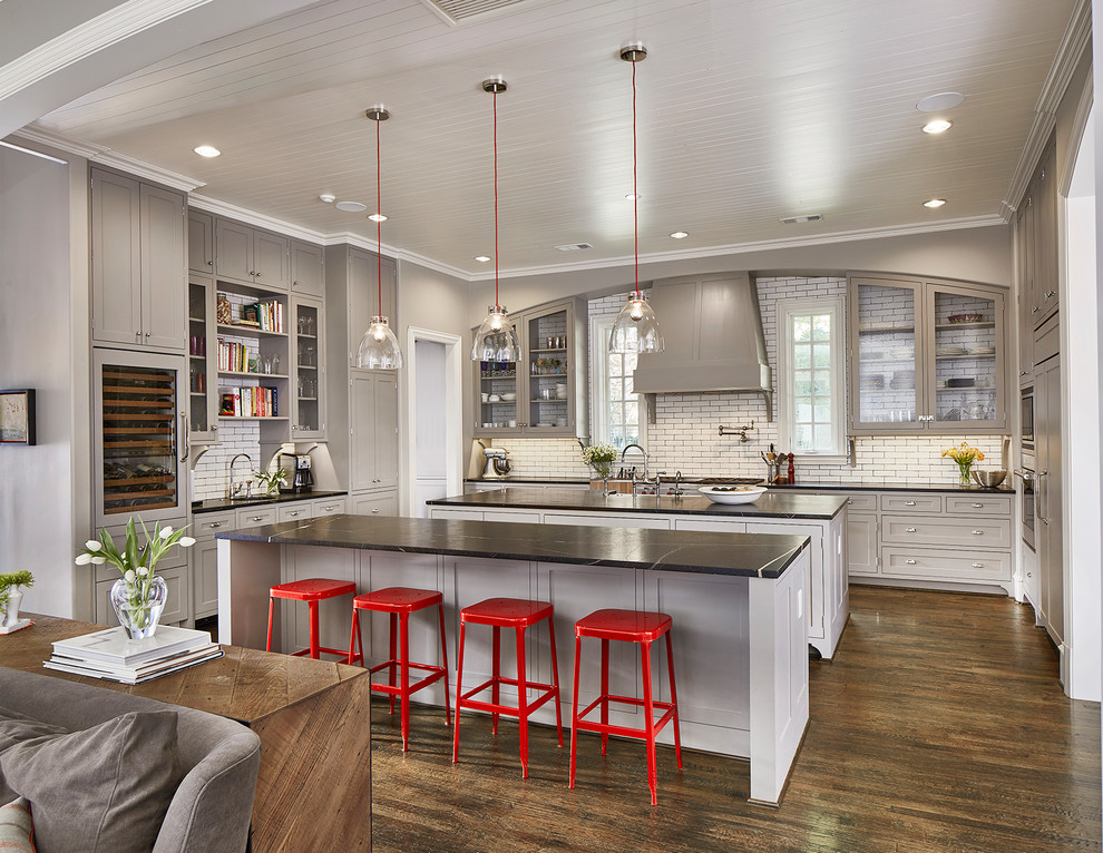 Kitchen - transitional u-shaped dark wood floor and brown floor kitchen idea in Dallas with a farmhouse sink, beaded inset cabinets, gray cabinets, soapstone countertops, white backsplash, subway tile backsplash, two islands and black countertops