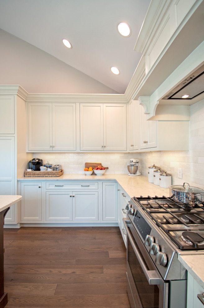 Transitional medium tone wood floor, brown floor and vaulted ceiling eat-in kitchen photo with shaker cabinets, white cabinets, quartz countertops, white backsplash, ceramic backsplash, stainless steel appliances, an island and white countertops