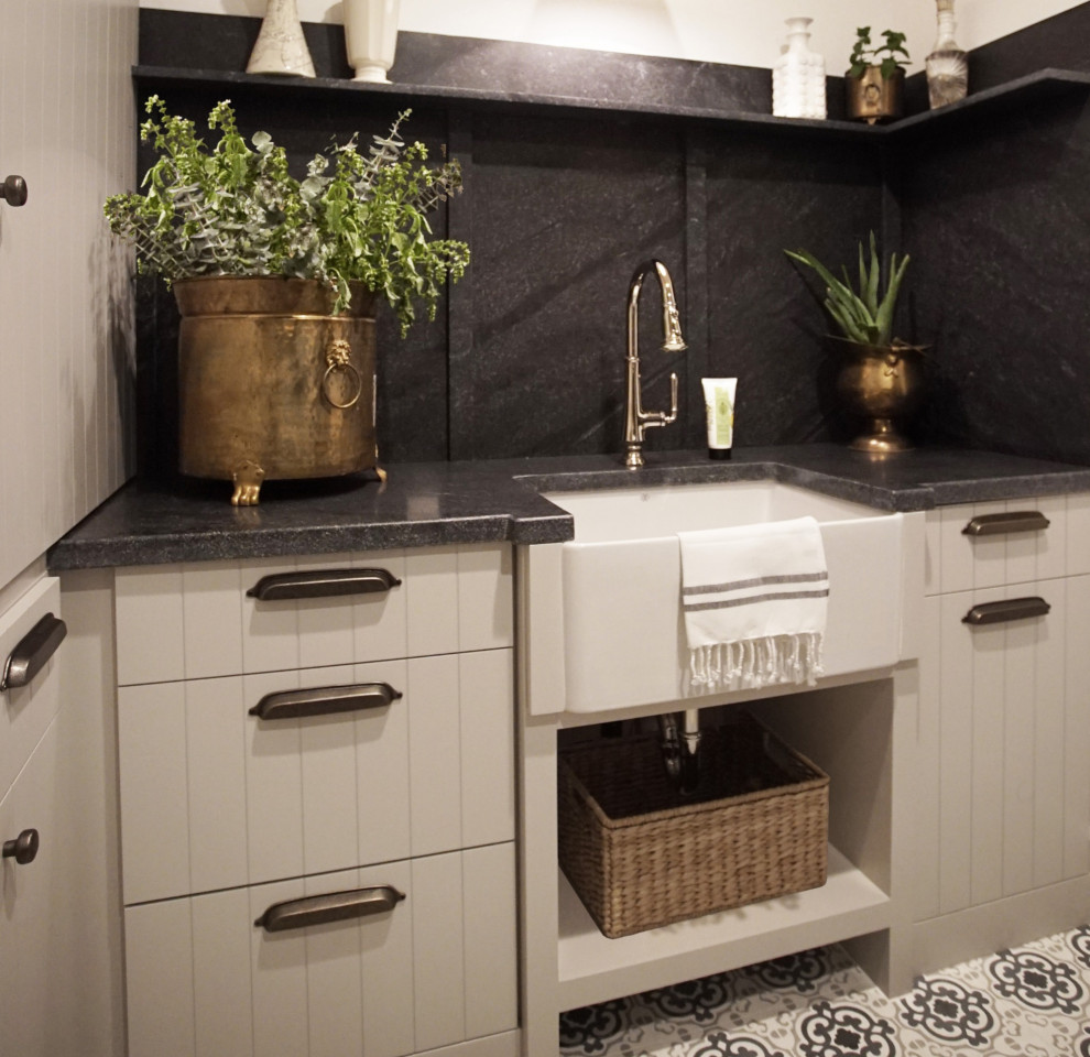 Inspiration for a mid-sized u-shaped dedicated laundry room in Phoenix with a farmhouse sink, flat-panel cabinets, grey cabinets, granite benchtops, black splashback, granite splashback, white walls, a side-by-side washer and dryer and black benchtop.