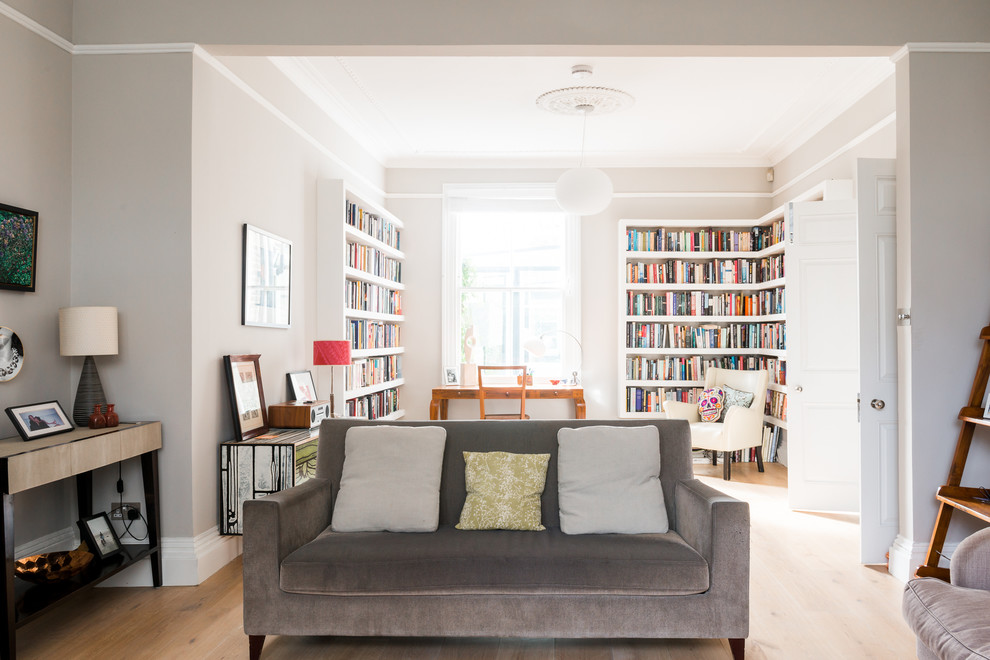 Large eclectic open concept living room in London with a library, grey walls, light hardwood floors, a standard fireplace, a stone fireplace surround and a freestanding tv.