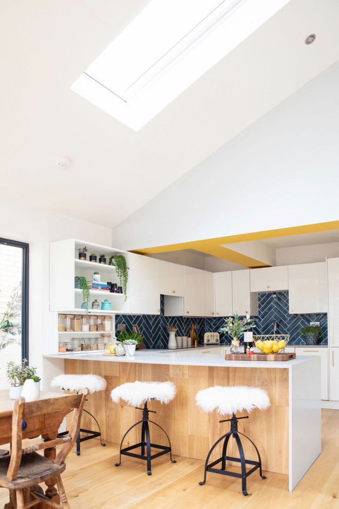 Large contemporary u-shaped eat-in kitchen in Hertfordshire with flat-panel cabinets, white cabinets, solid surface benchtops, blue splashback, panelled appliances, light hardwood floors, a peninsula, beige floor and white benchtop.