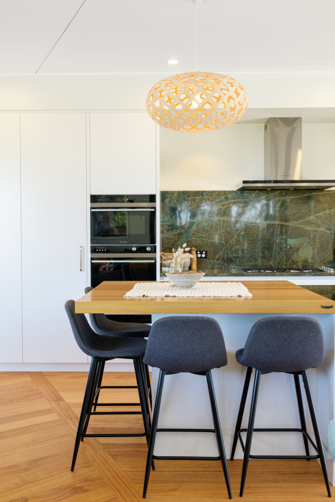 Modern inredning av ett grön linjärt grönt kök och matrum, med vita skåp, granitbänkskiva, grönt stänkskydd, stänkskydd i marmor, rostfria vitvaror, ljust trägolv och en köksö