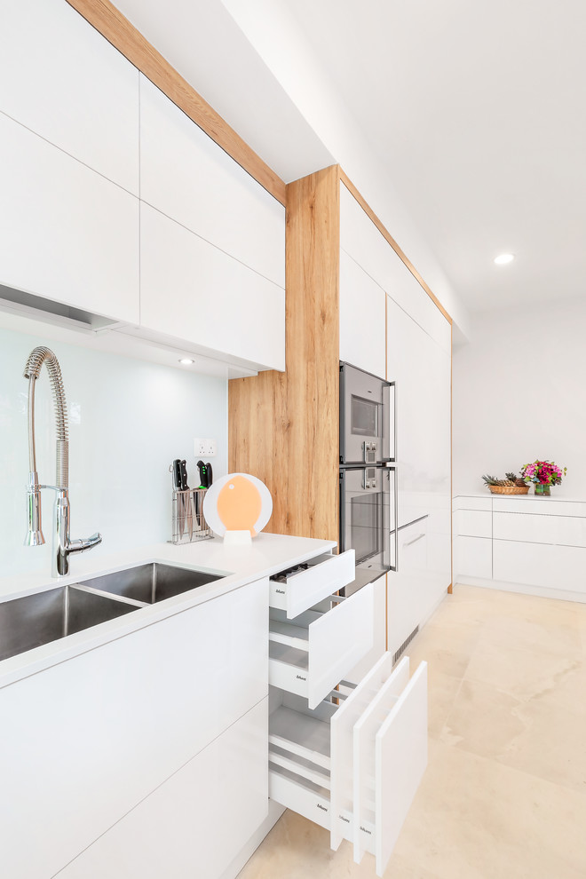 This is an example of a large scandinavian l-shaped eat-in kitchen in Singapore with an undermount sink, flat-panel cabinets, white cabinets, glass sheet splashback, stainless steel appliances and with island.