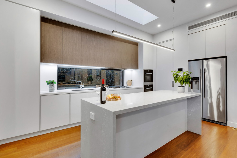 Inspiration for a mid-sized modern single-wall open plan kitchen in Melbourne with an undermount sink, flat-panel cabinets, white cabinets, quartz benchtops, window splashback, stainless steel appliances, with island and white benchtop.