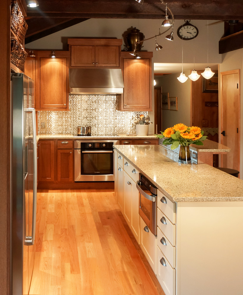 Inspiration for a rustic light wood floor kitchen remodel with an undermount sink, shaker cabinets, yellow cabinets, solid surface countertops, metallic backsplash and stainless steel appliances
