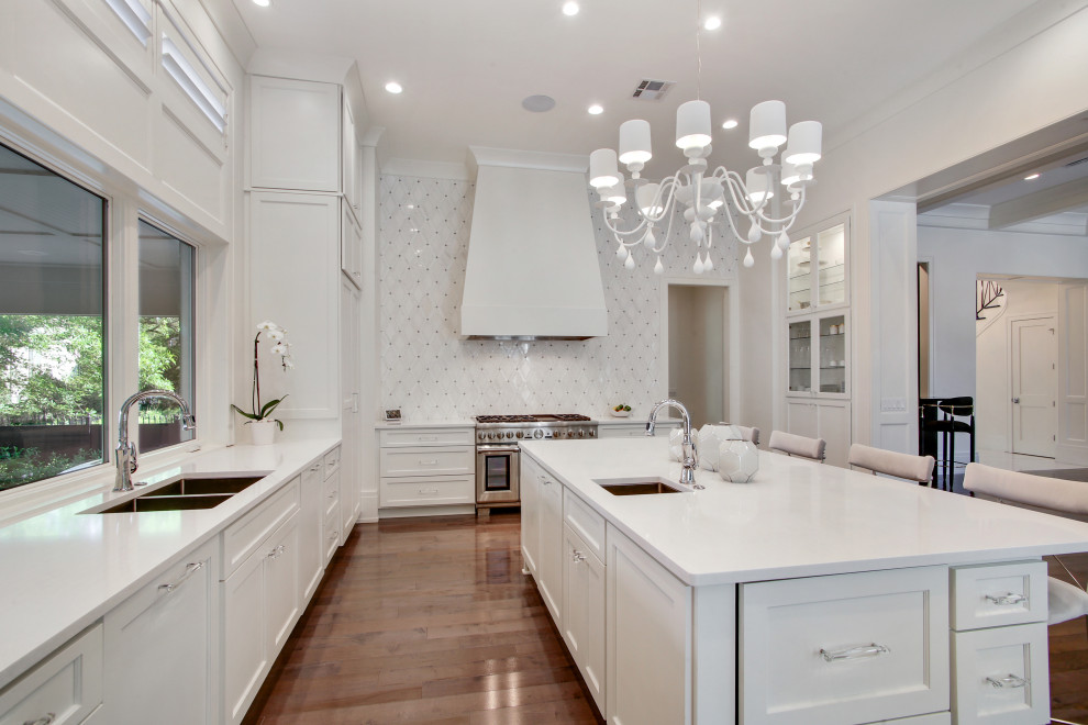 Large transitional galley kitchen in New Orleans with a double-bowl sink, shaker cabinets, white cabinets, wood benchtops, white splashback, ceramic splashback, stainless steel appliances, medium hardwood floors, with island, brown floor, white benchtop and vaulted.