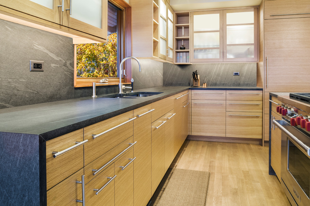 Photo of a contemporary l-shaped separate kitchen in Seattle with a double-bowl sink, flat-panel cabinets, light wood cabinets, granite benchtops, grey splashback, stone slab splashback, stainless steel appliances, light hardwood floors and with island.