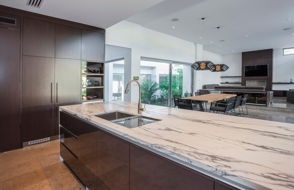 Photo of a large contemporary l-shaped eat-in kitchen in Perth with an undermount sink, flat-panel cabinets, metallic splashback, glass sheet splashback, stainless steel appliances, limestone floors and with island.